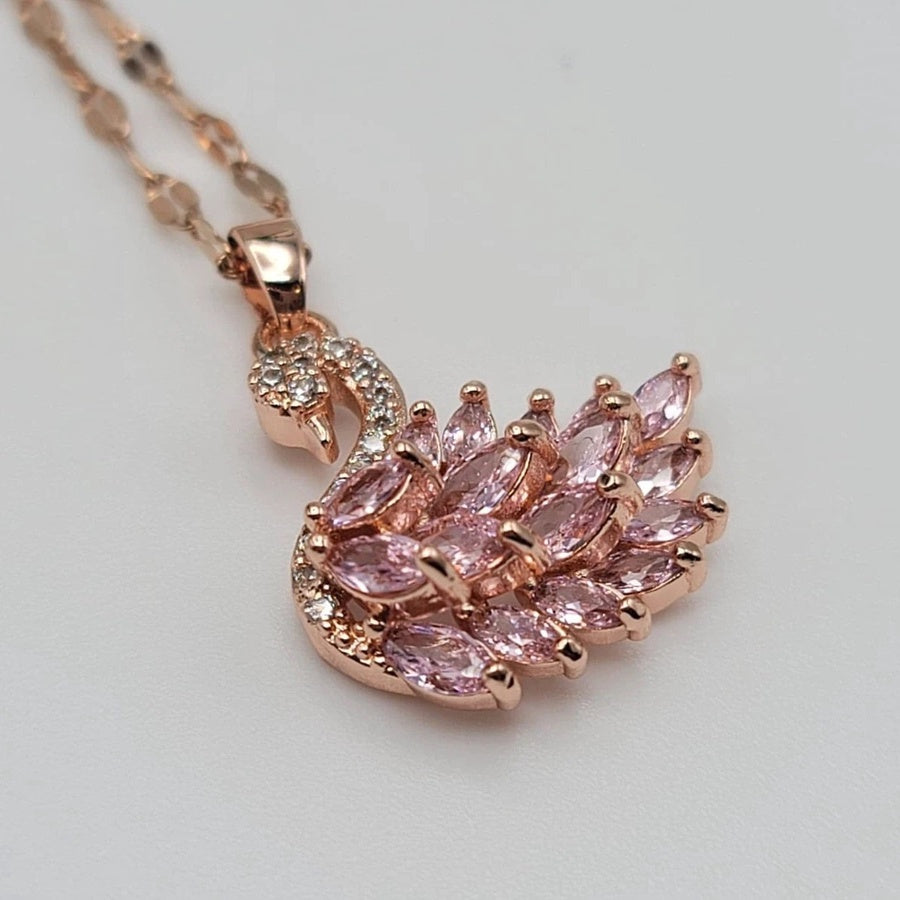 Rose gold necklace with pink gemstone swan pendant on a light gray background