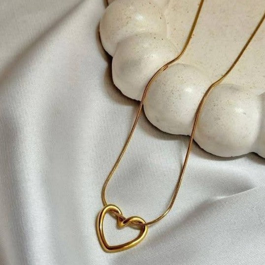 Gold necklace with a heart pendant held by a marble sculpture of hands.