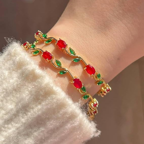 Gold bracelet with red and green stones on a wrist against a neutral background