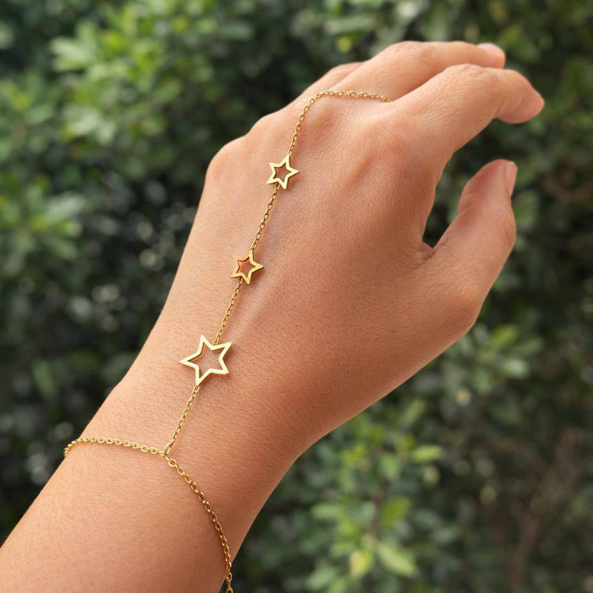 Gold star bracelet on a hand with a blurred green background