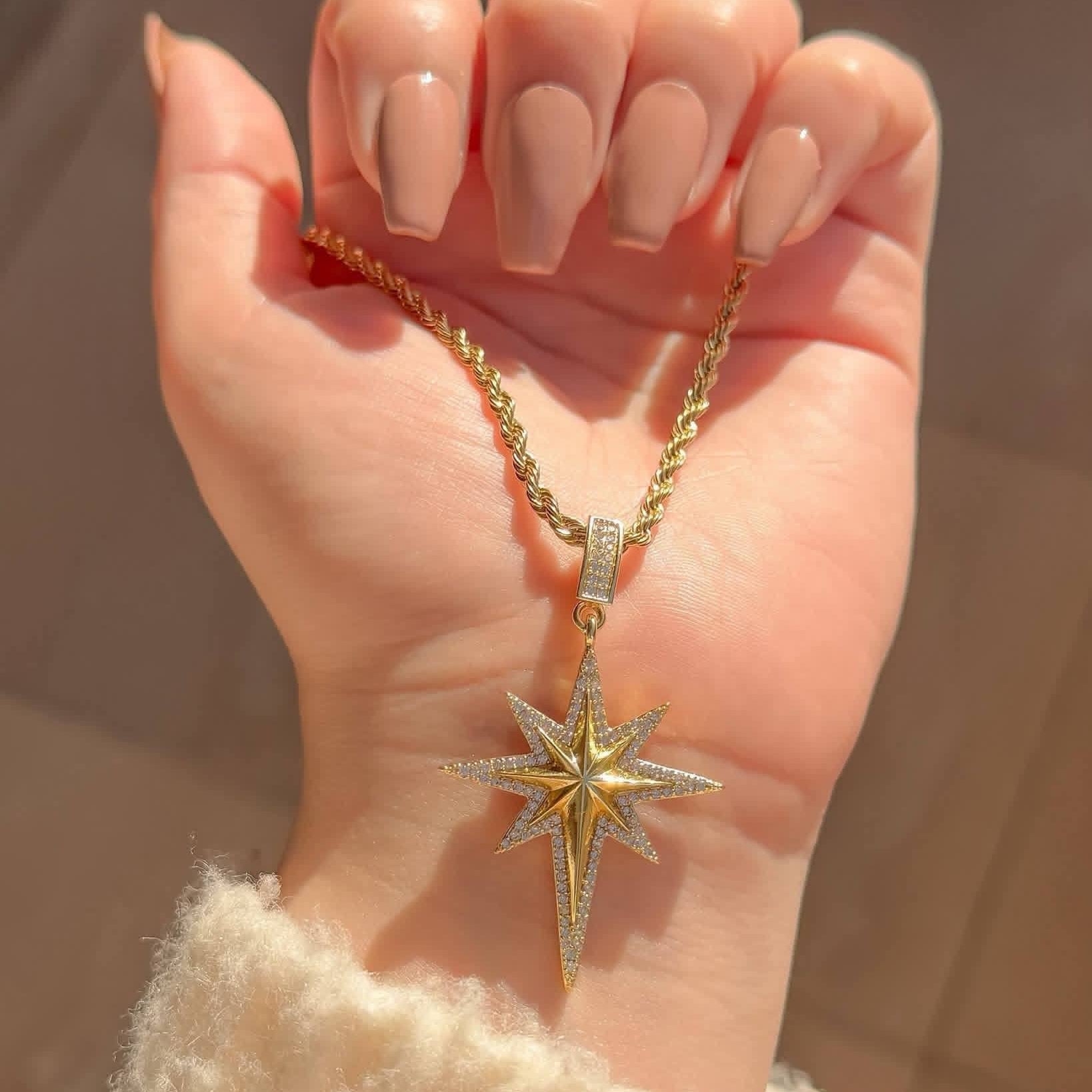 Gold star-shaped necklace on a hand with a neutral background