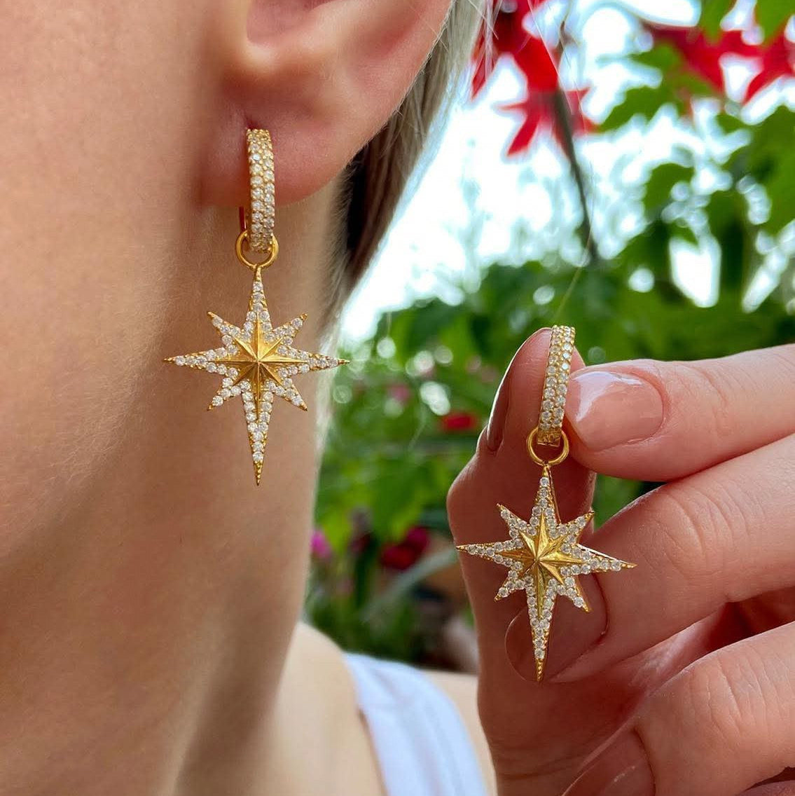 Gold star-shaped earrings worn by a person with a blurred natural background