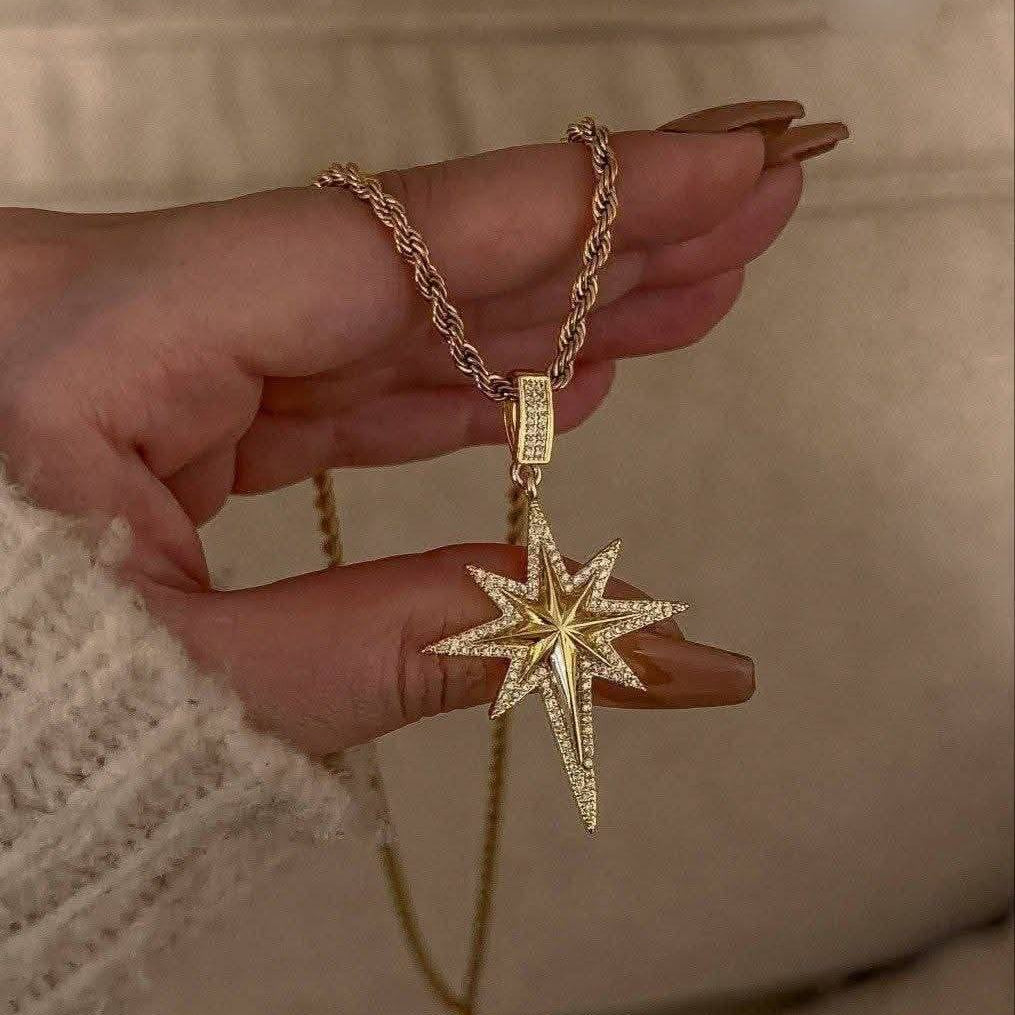 Gold necklace with a star-shaped pendant held by a hand against a neutral background