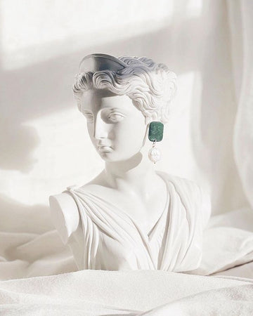 White classical statue with a green gemstone on a white background