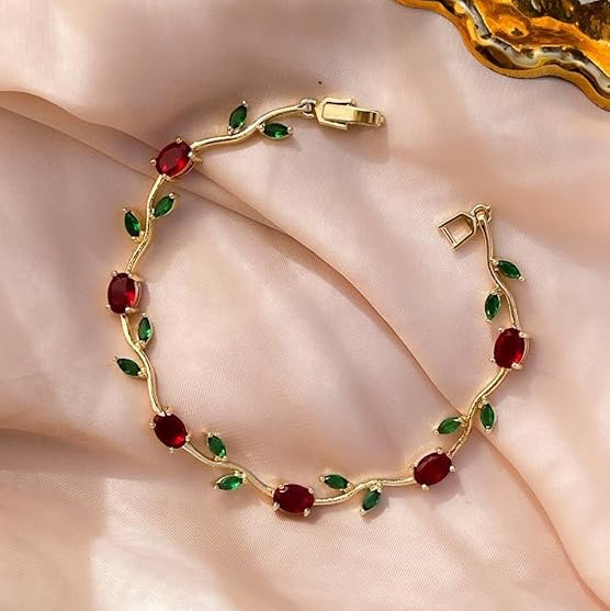 Gold bracelet with red and green gemstones on a soft pink fabric background