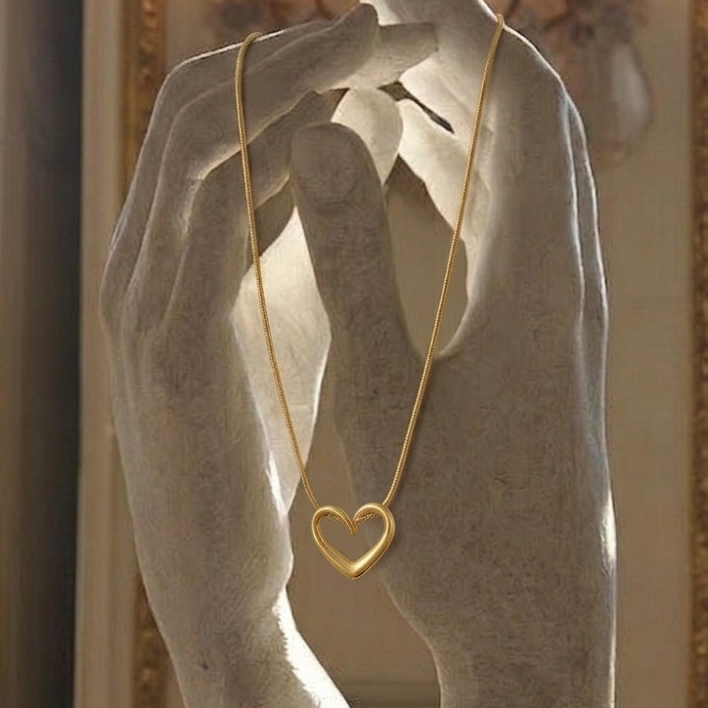 Gold necklace with a heart pendant held by a marble sculpture of hands.