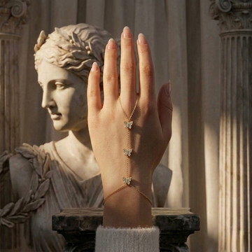 Hand wearing a gold bracelet with butterfly charms in front of a classical statue.
