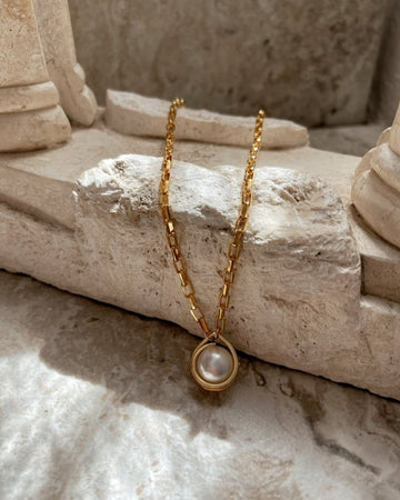 Gold necklace with a pearl pendant on a stone surface