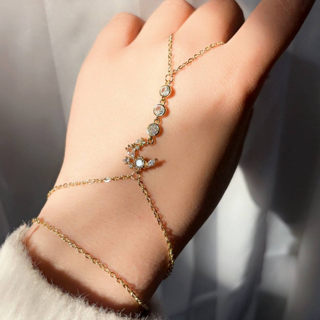 Hand wearing a gold bracelet with decorative elements against a classical architectural background