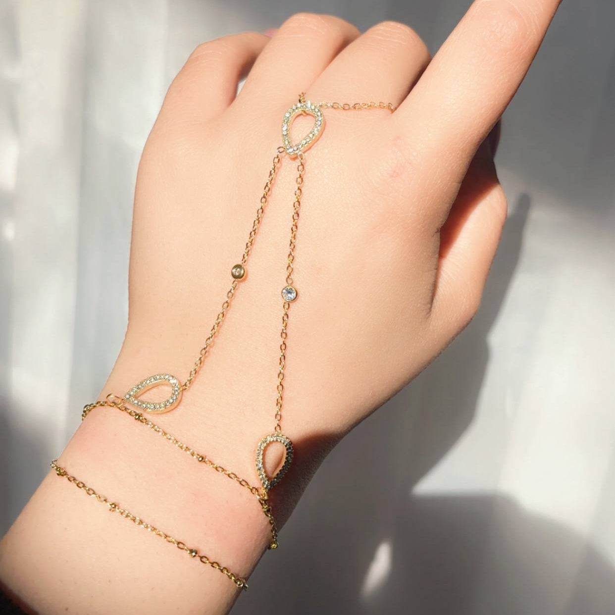 Gold bracelet with gemstones on a hand against a neutral background