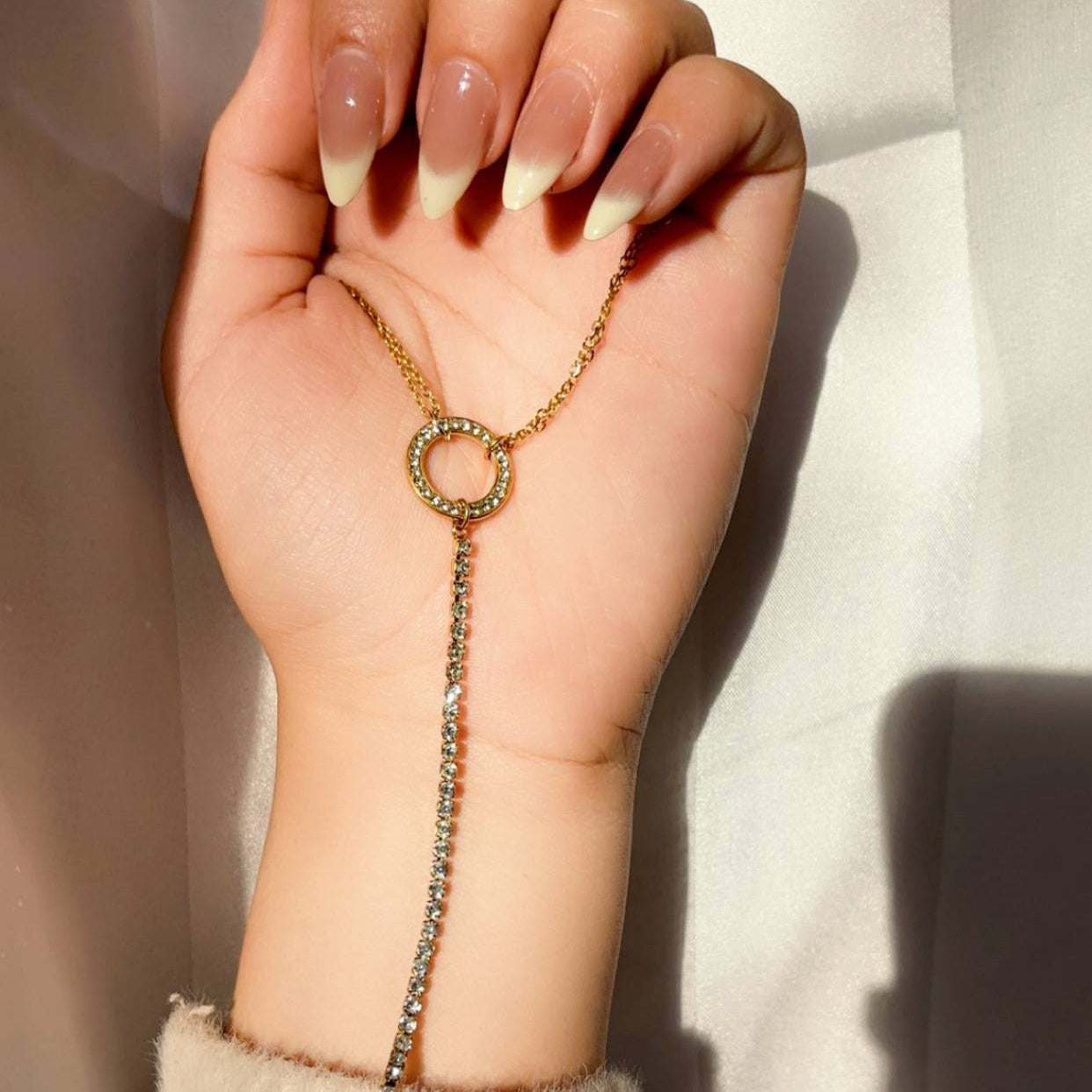 Hand wearing a delicate gold and gemstone bracelet on a neutral background