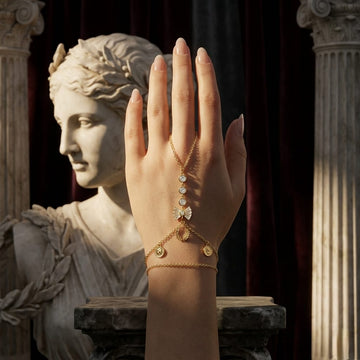 Hand wearing a gold bracelet with a statue in the background