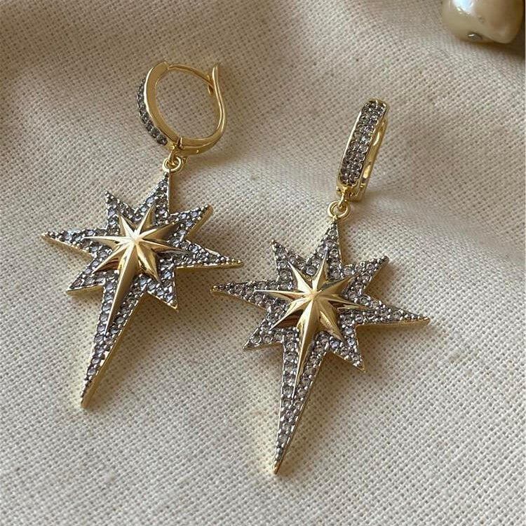 Gold star-shaped earrings on a beige fabric background