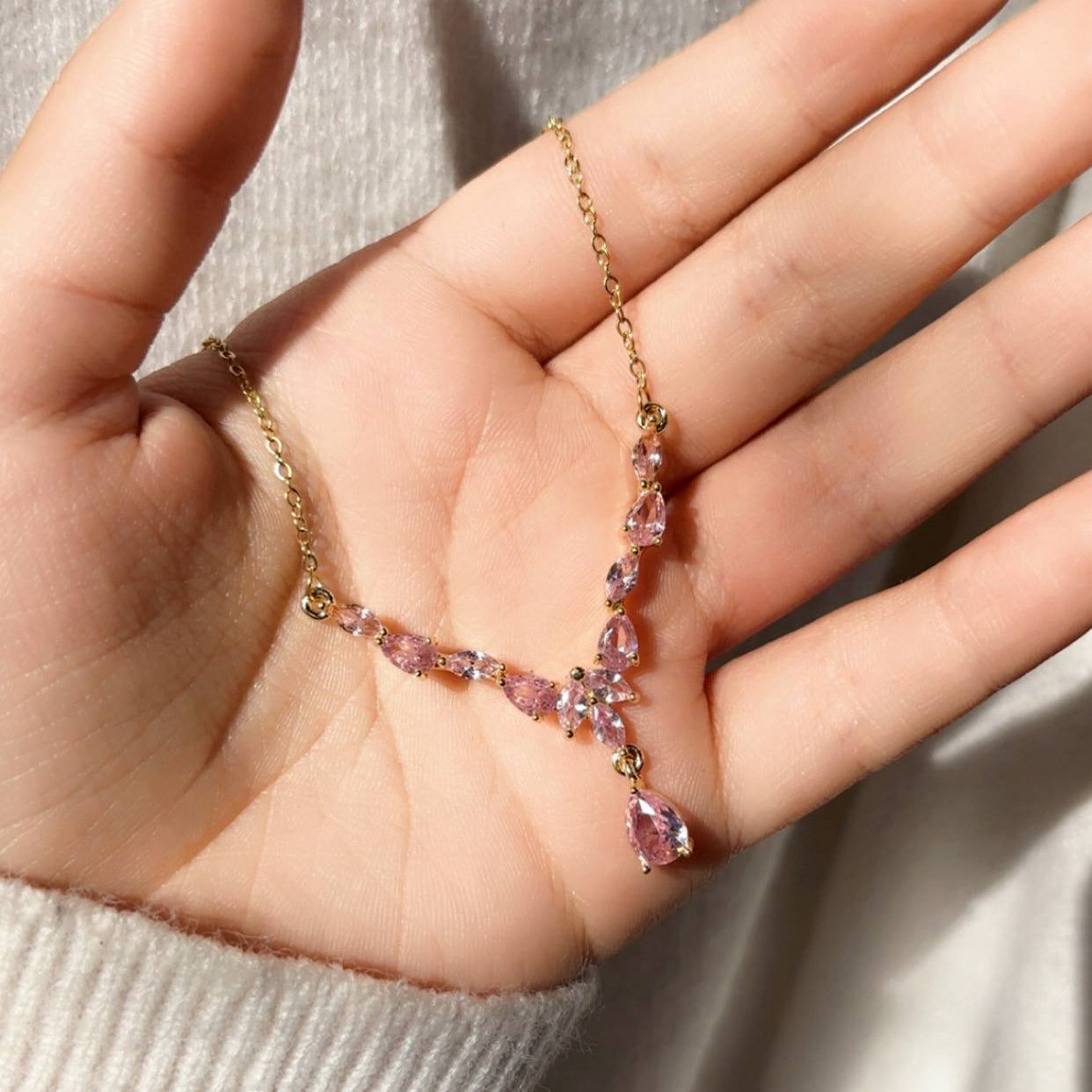 Hand holding a delicate necklace with pink gemstones against a neutral background