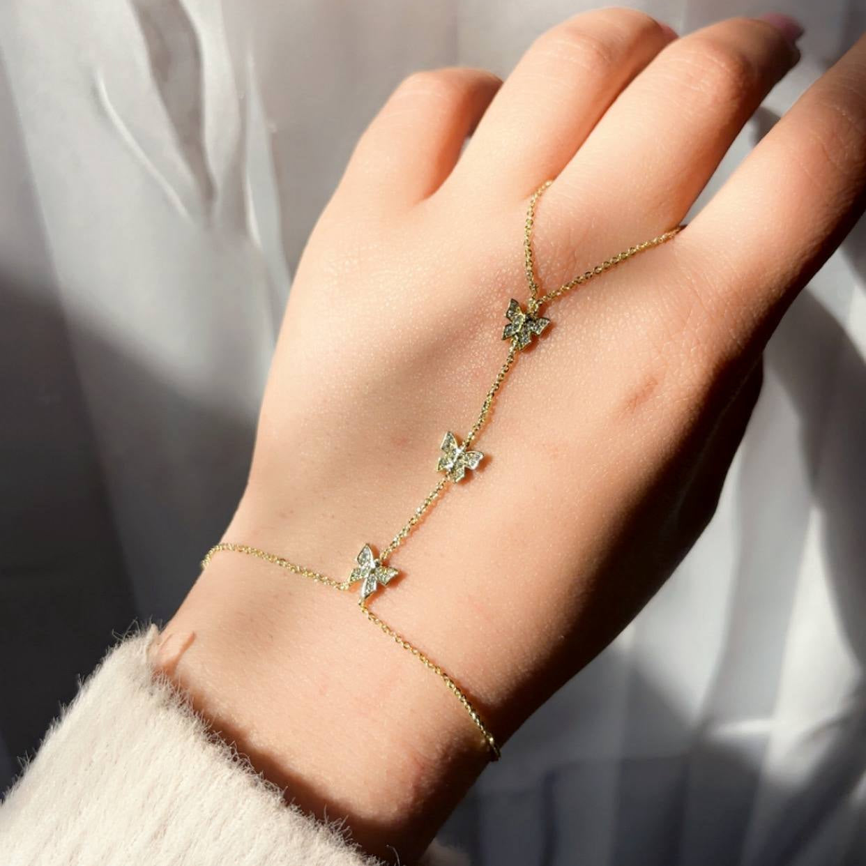 Gold bracelet with butterfly charms on a hand against a neutral background