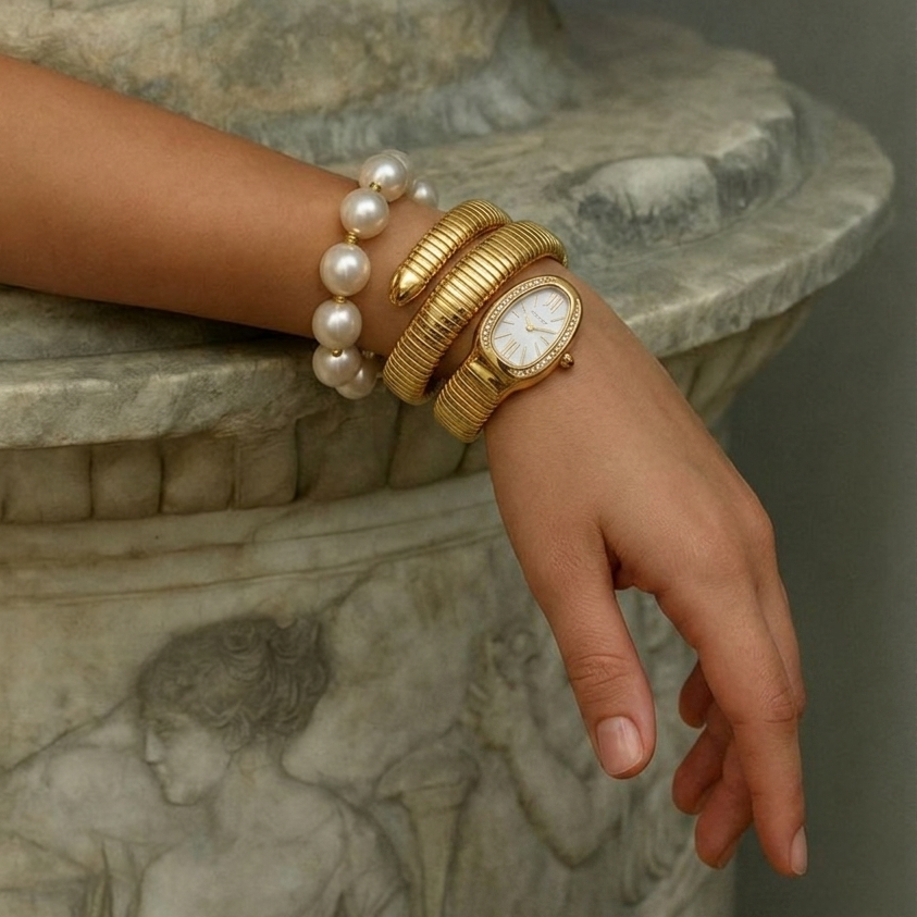 Hand wearing gold watch and pearl bracelet on decorative pedestal with 'Velveta' branding.